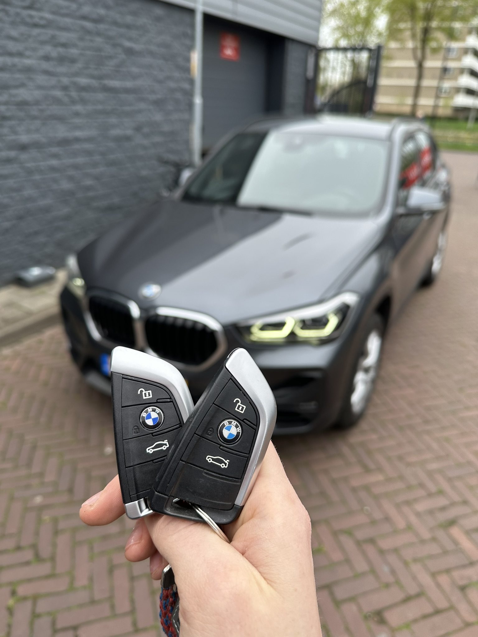 Twee BMW-smartkeys in de hand, met de BMW X1 op de achtergrond