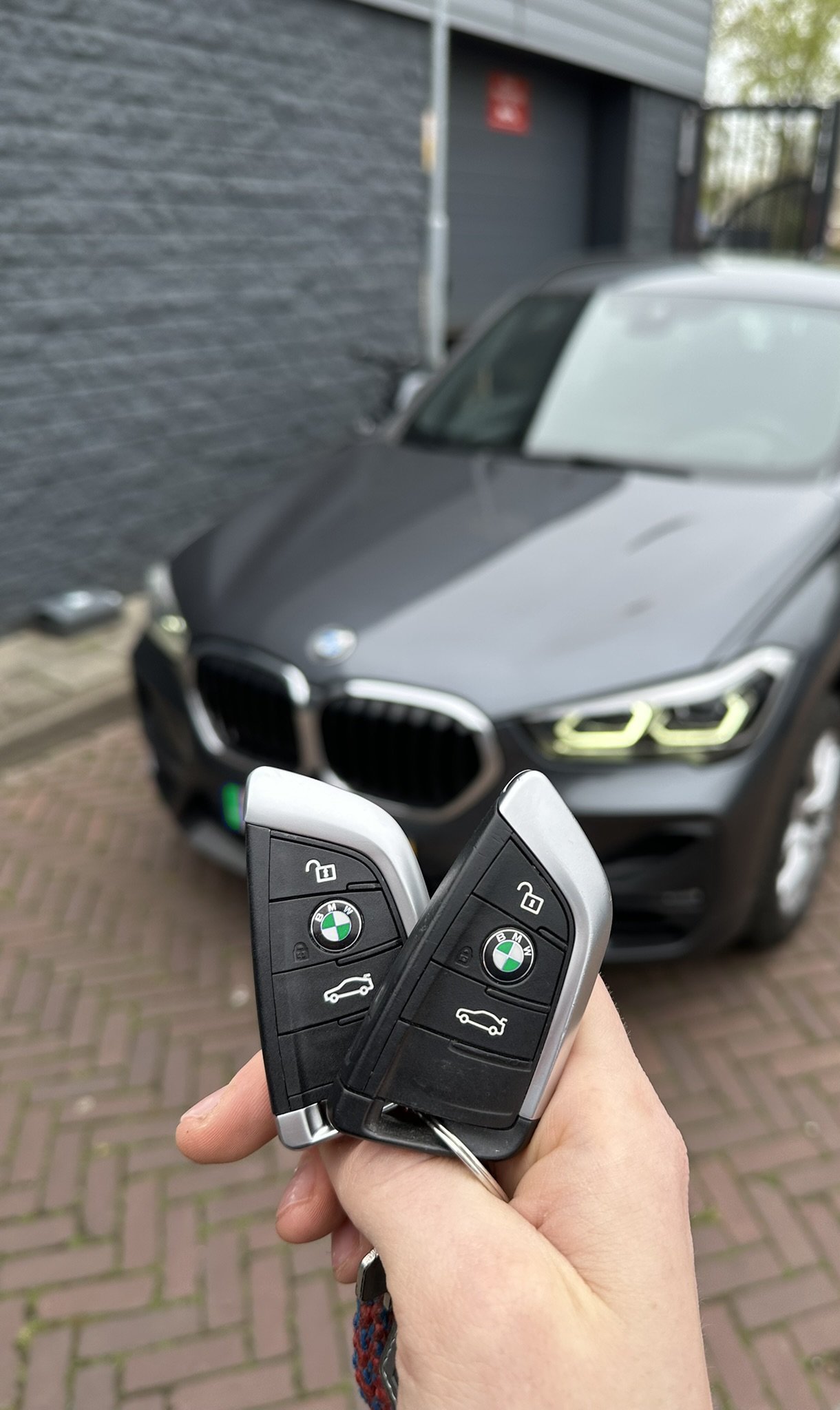 Twee bijgemaakte BMW-smartkeys in de hand, met de BMW X1 op de achtergrond