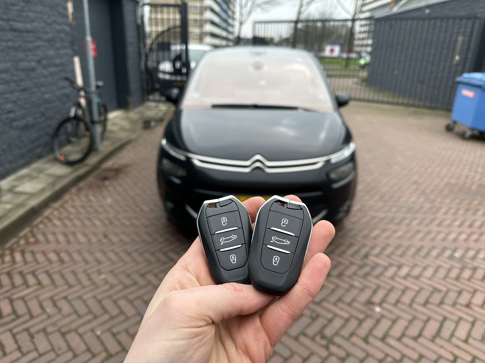 Twee Citroën-sleutels in de hand, met de Citroën C4 Picasso op de achtergrond