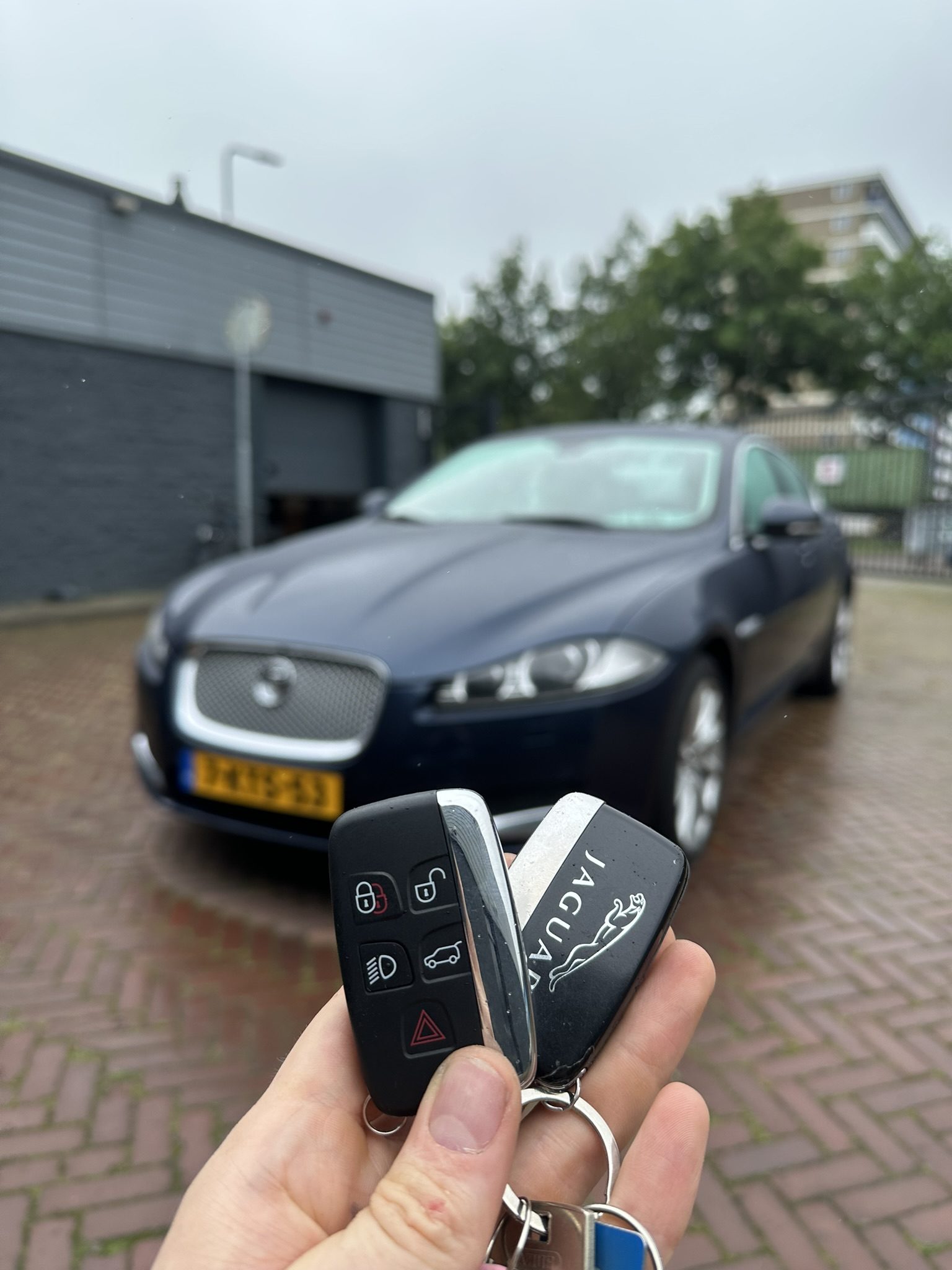 Twee Jaguar-smartkeys in de hand, met de Jaguar XF op de achtergrond
